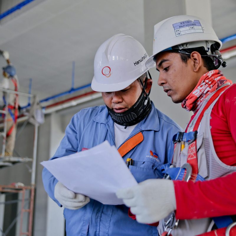 Two engineers in safety helmets reviewing construction plans at a worksite.