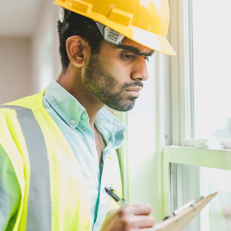 Professional construction worker examines property indoors with clipboard, ensuring safety compliance.